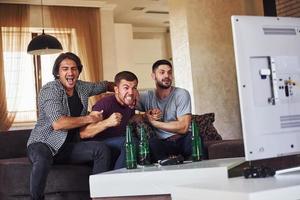 três amigos animados assistindo futebol na tv em casa juntos foto