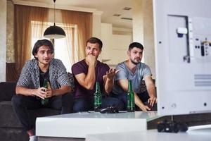 é uma derrota. tristes três amigos assistindo futebol na tv em casa juntos foto
