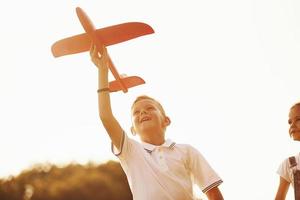 menina e menino se divertindo ao ar livre com avião de brinquedo vermelho nas mãos foto