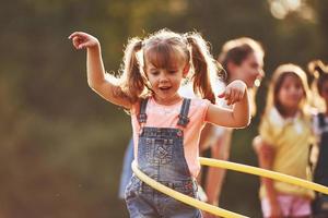 menina com ferramenta de fitness de círculo. grupo de crianças tem fim de semana ativo no campo. iluminado pela bela luz do sol foto