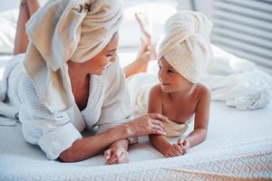 jovem mãe com sua filha tem dia de beleza dentro de casa no quarto branco foto