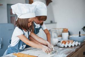 concentrando-se em cozinhar. filhos de família em uniforme de chef branco preparando comida na cozinha foto