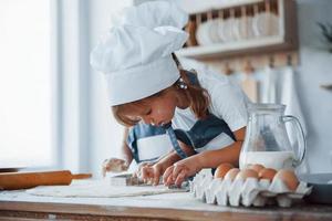 concentrando-se em cozinhar. filhos de família em uniforme de chef branco preparando comida na cozinha foto