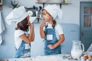 se divertindo com espaguete. filhos de família em uniforme de chef branco preparando comida na cozinha foto