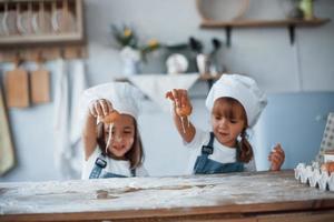 brincando com ovos. filhos de família em uniforme de chef branco preparando comida na cozinha foto