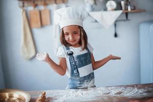 se divertindo. garoto bonito em uniforme de chef branco preparando comida na cozinha foto