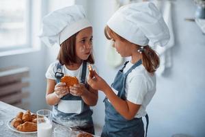 crianças de família em uniforme de chef branco comem comida na cozinha foto