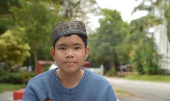 retrato asiático muçulmano ou menino islâmico sentado no parque da escola e sorrindo alegremente, foco suave e seletivo. foto