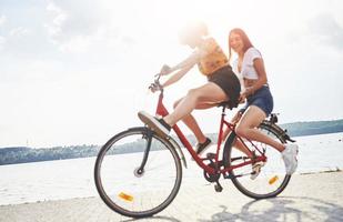 duas amigas na bicicleta se divertem na praia perto do lago foto