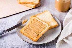 torrada de pão com manteiga de amendoim em um prato e um pote de manteiga na mesa foto