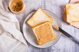 sanduíche de manteiga de amendoim no pão torrado em um prato e pote de manteiga na mesa. vista do topo foto