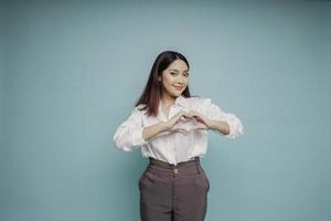 uma jovem asiática feliz vestindo uma camisa branca sente formas românticas gesto do coração expressa sentimentos ternos foto