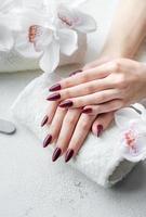 mãos de uma jovem com manicure vermelho escuro nas unhas foto