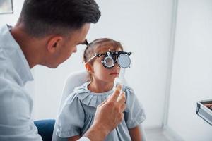 testando a visão. jovem oftalmologista está com pequena visitante feminina na clínica foto