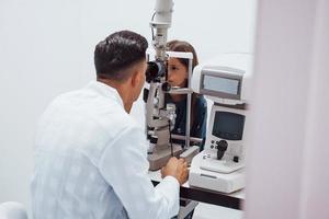 jovem oftalmologista está com pequena visitante feminina na clínica foto
