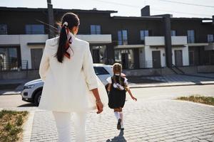 mãe com filha em uniforme escolar ao ar livre perto de carro branco foto