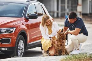 senta-se com animal de estimação. lindo casal tem um passeio junto com cachorro ao ar livre perto do carro foto