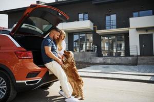 porta-malas está aberto. lindo casal tem um passeio junto com cachorro ao ar livre perto do carro foto