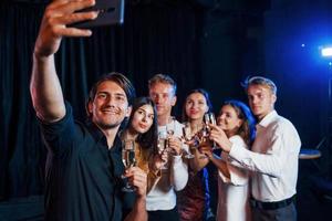 tira selfie. grupo de amigos alegres comemorando o ano novo dentro de casa com bebidas nas mãos foto