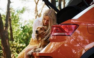 senta na parte de trás do carro. mulher com seu cachorro ao ar livre na floresta se diverte foto