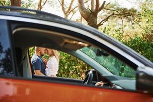 casal se abraçando na floresta perto de carro moderno foto