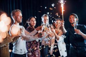 copos batendo. grupo de amigos alegres comemorando o ano novo dentro de casa com bebidas nas mãos foto