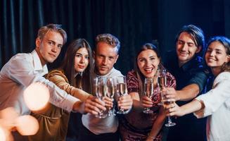 copos batendo. grupo de amigos alegres comemorando o ano novo dentro de casa com bebidas nas mãos foto