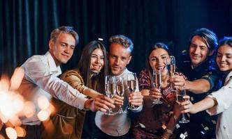 copos batendo. grupo de amigos alegres comemorando o ano novo dentro de casa com bebidas nas mãos foto