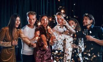 se divertindo com estrelinhas. grupo de amigos alegres comemorando o ano novo dentro de casa com bebidas nas mãos foto