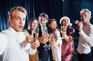 tira selfie. grupo de amigos alegres comemorando o ano novo dentro de casa com bebidas nas mãos foto