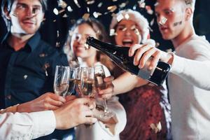 derramando champanhe. grupo de amigos alegres comemorando o ano novo dentro de casa com bebidas nas mãos foto
