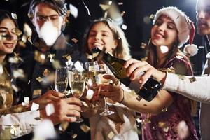 derramando champanhe. grupo de amigos alegres comemorando o ano novo dentro de casa com bebidas nas mãos foto