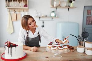 loira positiva com seus deliciosos biscoitos caseiros e bolo na cozinha foto