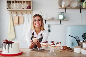 loira positiva com seus deliciosos biscoitos caseiros e bolo na cozinha foto