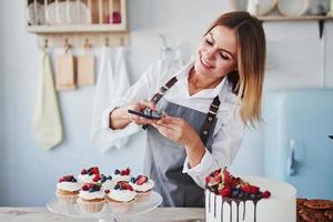 mulher fica na cozinha e tira foto de seus biscoitos caseiros e torta usando telefone