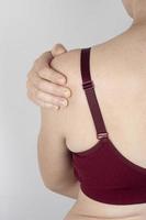 mulher em um sutiã esportivo segurando seu ombro dolorido, tendões esticados do antebraço foto