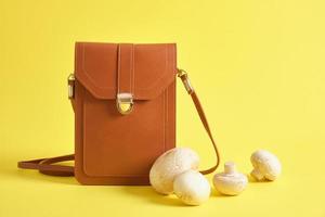 bolsa marrom de couro ecológico e cogumelos em um fundo amarelo, conceito de couro de micélio foto