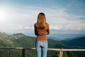 imagem de visão traseira de uma mulher viajante sentada e olhando para uma bela montanha, campo de flores e vista da natureza foto