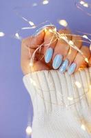 unhas aconchegantes com manicure de inverno com flocos de neve e luzes no fundo roxo foto