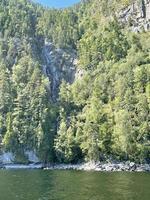 um fluxo fino de uma cachoeira em uma rocha perto de um lago teletskoye em dia ensolarado. altai, rússia. foto