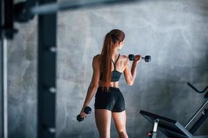 mulher jovem fitness com corpo magro e em roupas esportivas pretas está no ginásio foto
