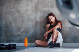 mulher jovem fitness senta-se no chão com água no ginásio