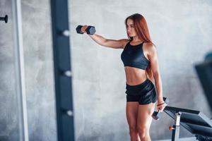 mulher jovem fitness está no ginásio com halteres nas mãos foto