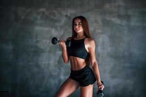 mulher jovem fitness está no ginásio perto da parede com halteres nas mãos foto