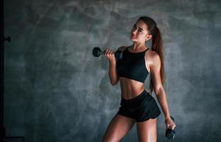 mulher jovem fitness está no ginásio perto da parede com halteres nas mãos