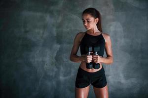 mulher jovem fitness está no ginásio perto da parede com halteres nas mãos foto