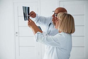 médicos de homem e mulher sênior em uniforme branco examinam o raio-x das pernas humanas foto