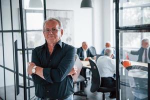 retrato de um homem sênior que fica na frente de uma equipe de arquitetos de empresários idosos que têm uma reunião no escritório foto