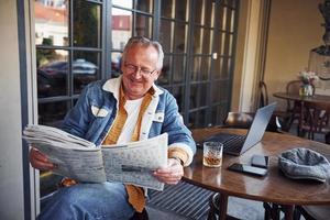 elegante sênior em roupas da moda e óculos senta-se no café e lê jornal foto