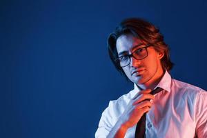 homem bonito com roupa formal e óculos está no estúdio com iluminação neon azul foto